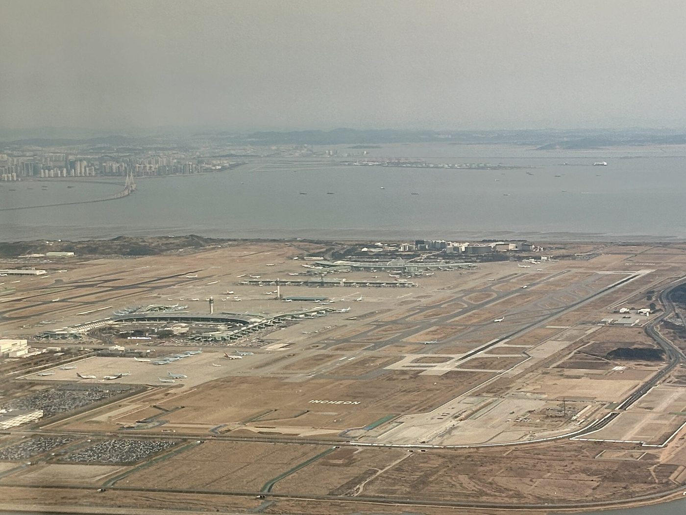 이륙하는 항공기에서 내려다본 인천공항. 매립지 위의 터미널과 활주로, 바다 건너 송도