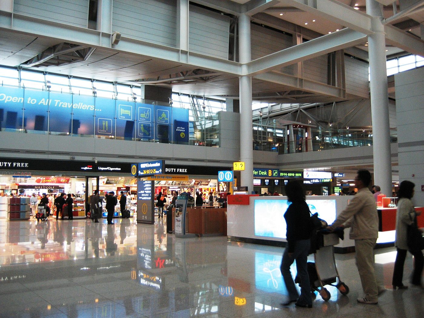 인천공항 제1여객터미널 보딩 로비의 면세 구역. 높은 천장 아래 면세점 간판과 매장, 카트를 미는 여행객들