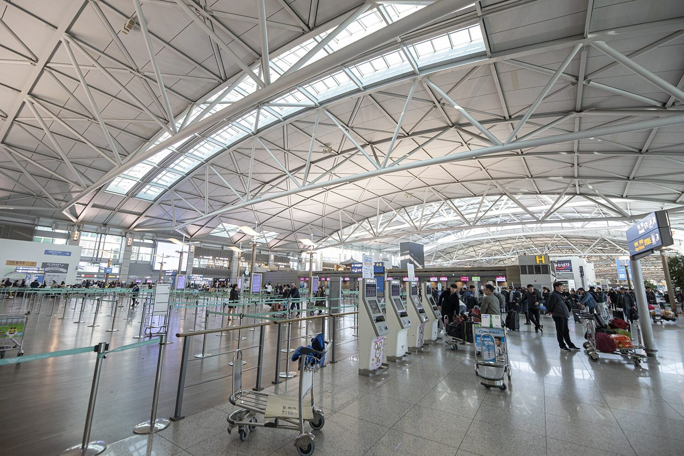 인천공항 제1여객터미널 출국장. 흰 트러스 지붕 아래 체크인 카운터와 여행객들
